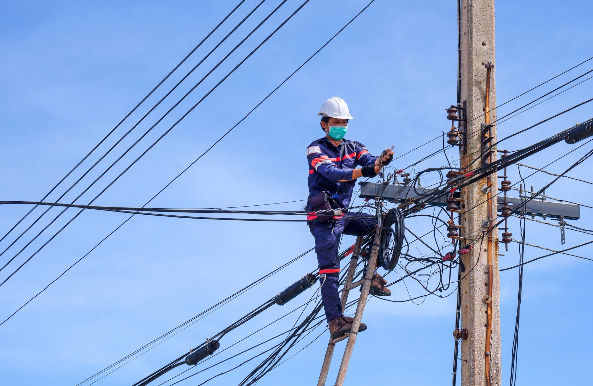 technician on wooden ladder installing internet fiber optic line on electric pole against blue sky